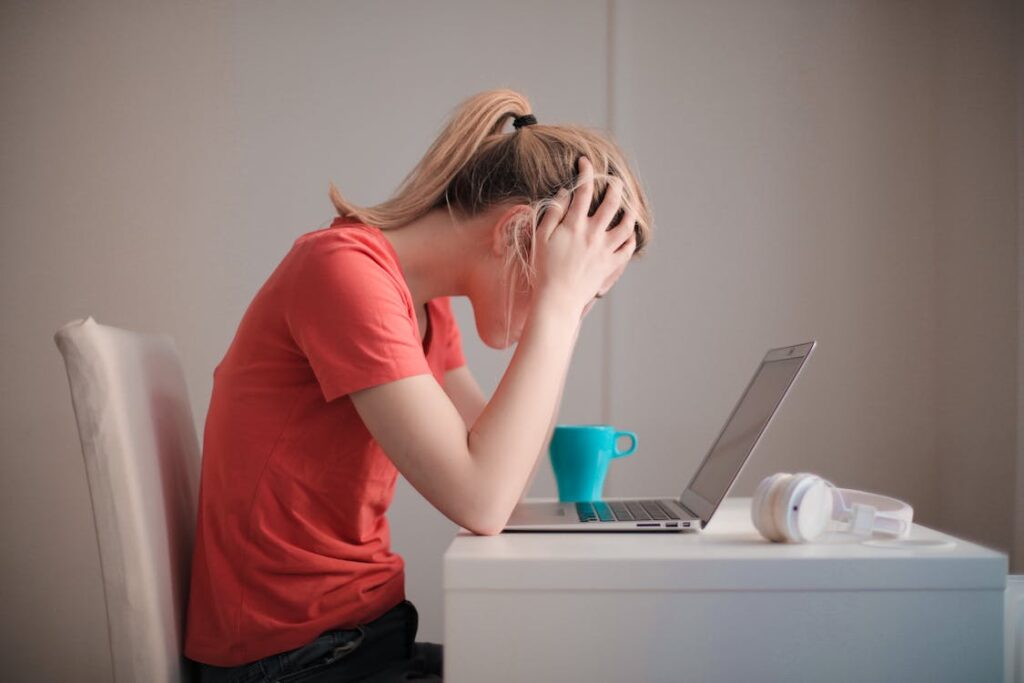 Stressed student sitting at a desk and looking at a laptop while holding their head