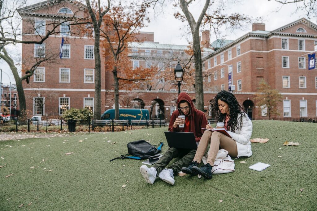 Two students sitting on green grass in a college yard