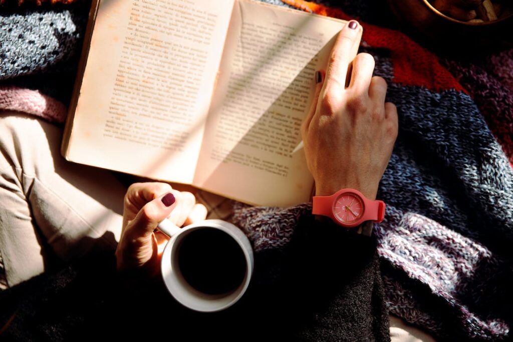 A person holding a cup of tea and reading a book 