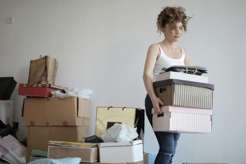 A woman with curly hair packing boxes in preparation for a college move with a limited budget, surrounded by various boxes.