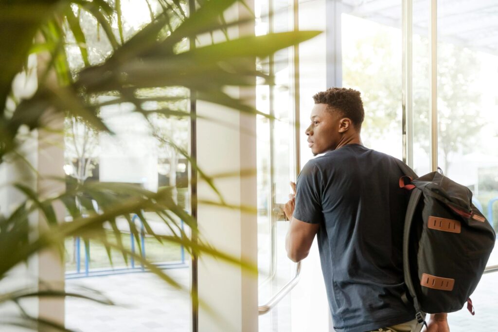 Man in a black shirt with a backpack opening a glass door.